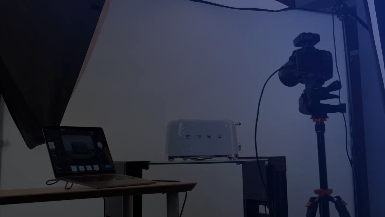Set de fotografía de producto con tethering: una notebook con el software de captura junto a una cámara en trípode y un producto sobre un estante de vidrio