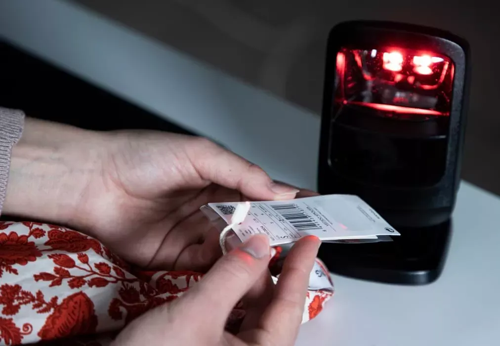 Primer plano de manos escaneando la etiqueta con código de barras de una prenda para inventario