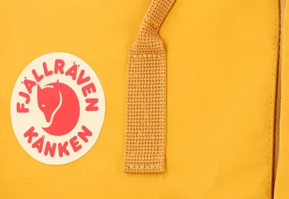 Primer plano del logo y la correa de una mochila Kanken amarilla