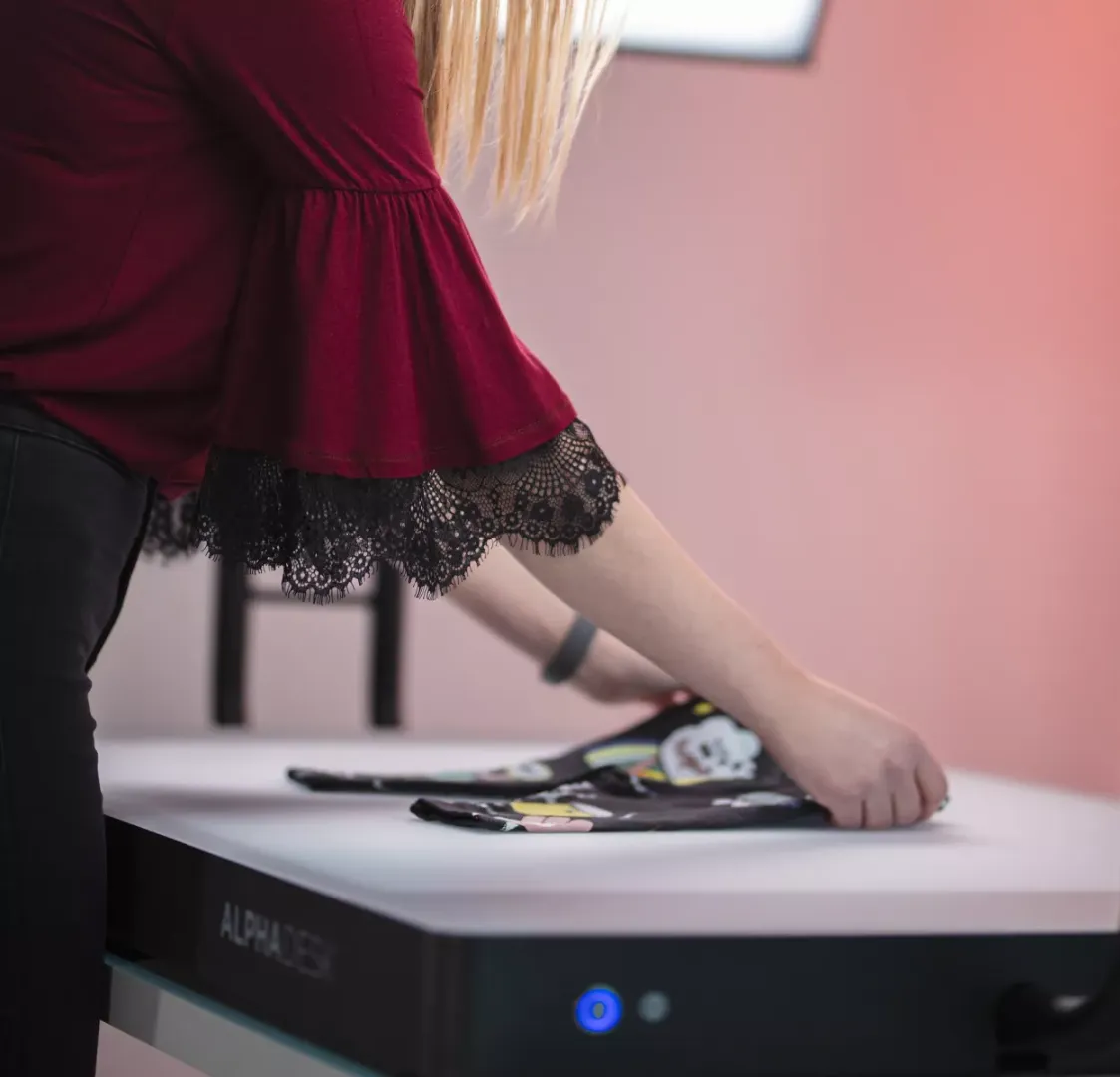 Mujer doblando ropa infantil en un escritorio blanco con Alphadesk
